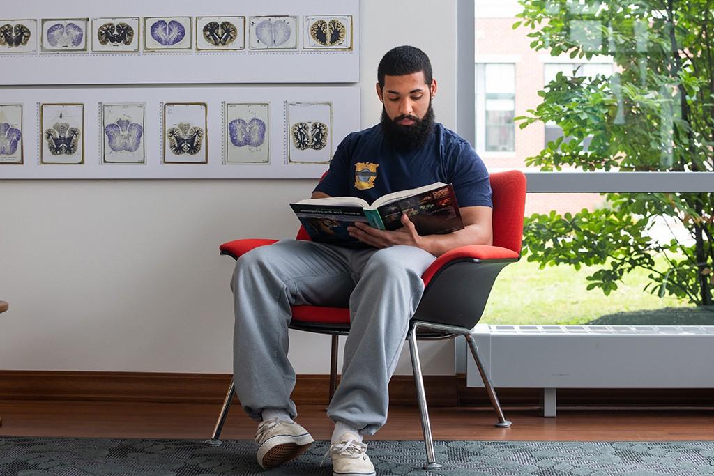 A U N E student read a book while sitting in a chair in front of an art display