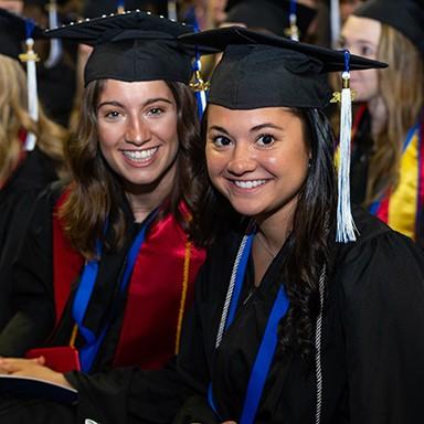 Two College of Arts and Science undergraduate students sitting together at their commencement ceremony