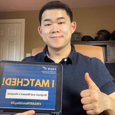 A man poses for a selfie holding a tablet displaying the words "I Matched!" while giving a thumbs up